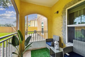 A balcony with a view of a yellow building, a wicker sofa, a small table with a lantern, and a potted plant. - Ground floor 2 Bedroom One Bathroom Condo in gated community with Pool (Seminole)