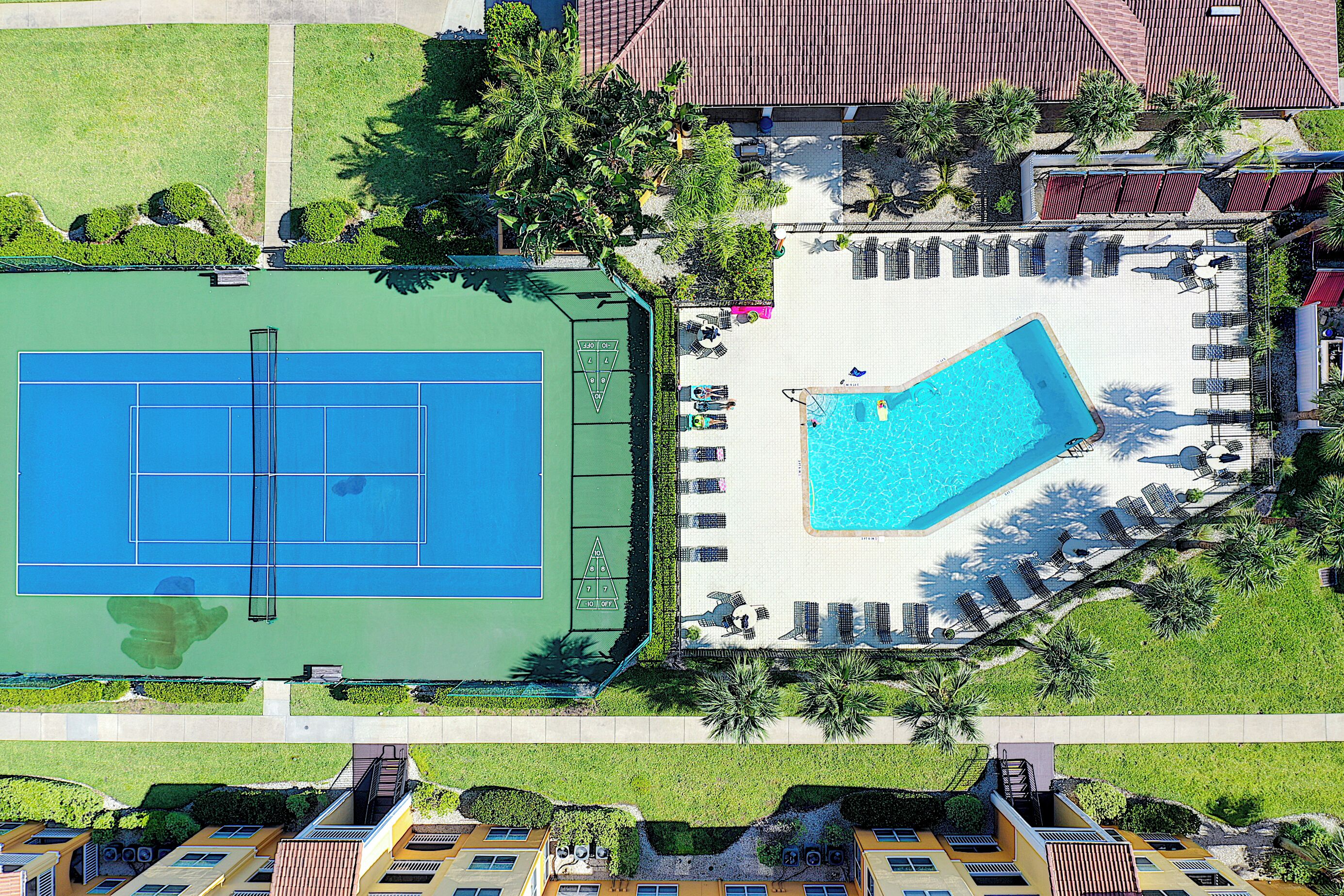 Eine Dachterrasse mit Tennisplatz und Schwimmbecken, umgeben von Grünflächen und Gebäuden.