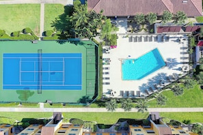 Una azotea con cancha de tenis y piscina, rodeada de vegetación y edificios.