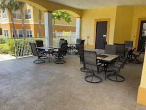 An outdoor patio area with tables and chairs, a railing, and a building in the background.