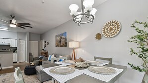 Un coin repas avec une table dressée pour quatre personnes, un ventilateur de plafond et une cuisine en arrière-plan.