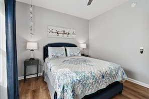 A bedroom with a bed, two bedside tables, a ceiling fan, and a wall-mounted artwork.