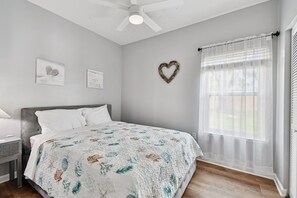A bedroom with a bed, a ceiling fan, a window with sheer curtains, and wall art. - Ground floor 2 Bedroom One Bathroom Condo in gated community with Pool (Seminole)
