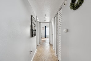 A hallway with white walls, a tiled floor, and a door at the end leading to another room.