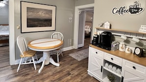 Ein Essbereich mit einem runden Tisch und Stühlen, einer Kaffeestation mit Kaffeemaschine und einem gerahmten Bild an der Wand.