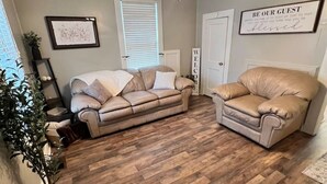 Ein Wohnzimmer mit Holzboden, Deckenventilator, Sofa, Sessel und einem an der Wand befestigten Schild.
