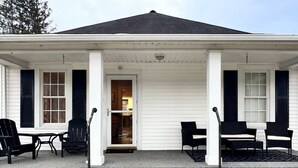 Ein Haus mit Veranda, weißem Farbanstrich und schwarzen Fensterläden. Auf der Veranda stehen zwei Sitzgruppen.