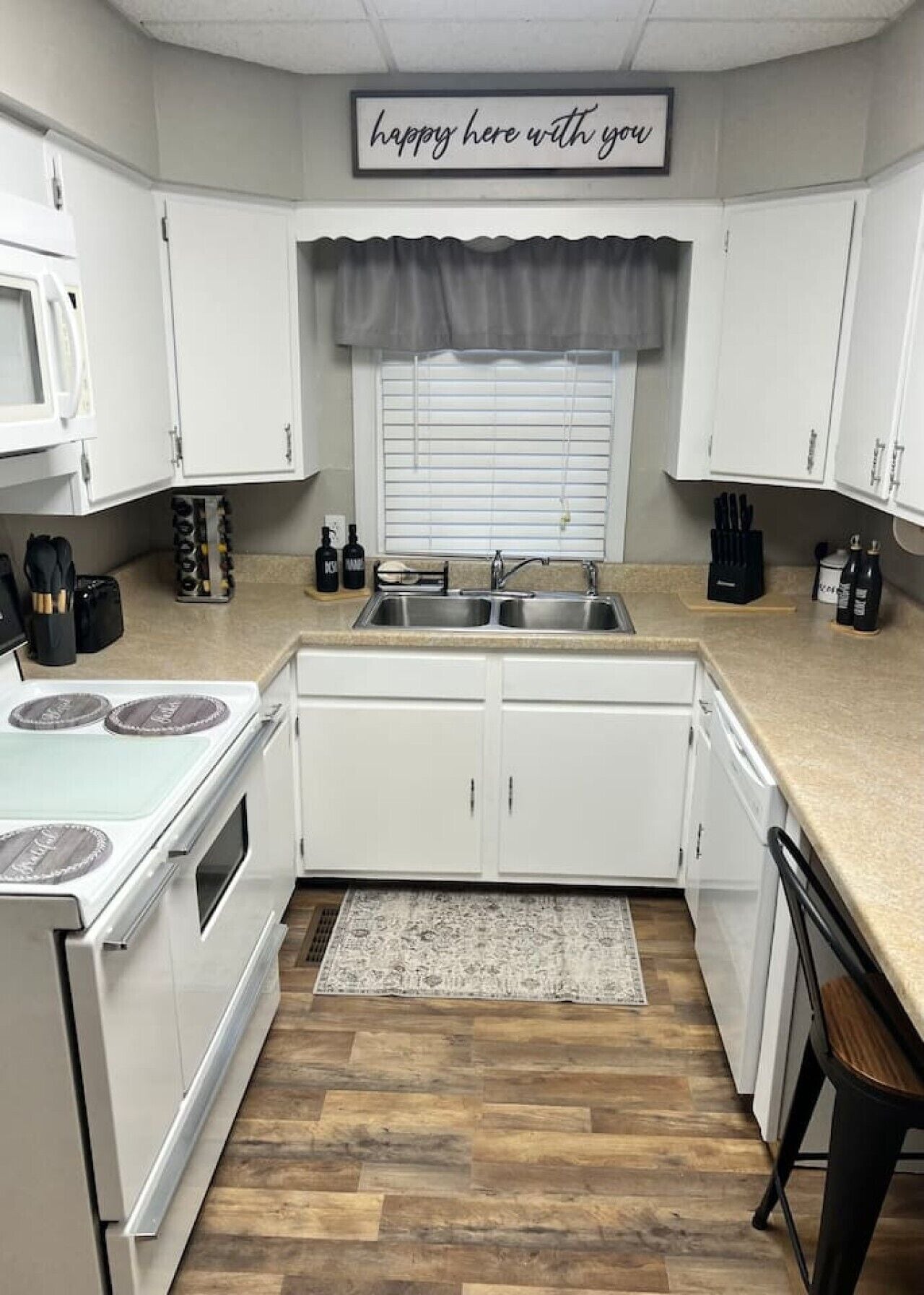 A kitchen with white cabinets, a stove, a sink, and a window with blinds.