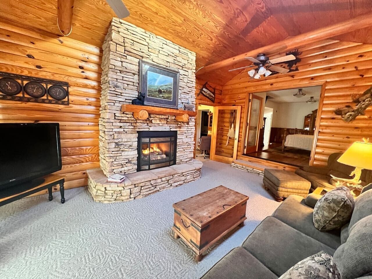 L’intérieur d’un chalet en bois, avec une cheminée en pierre, un téléviseur et un coin salon confortable.