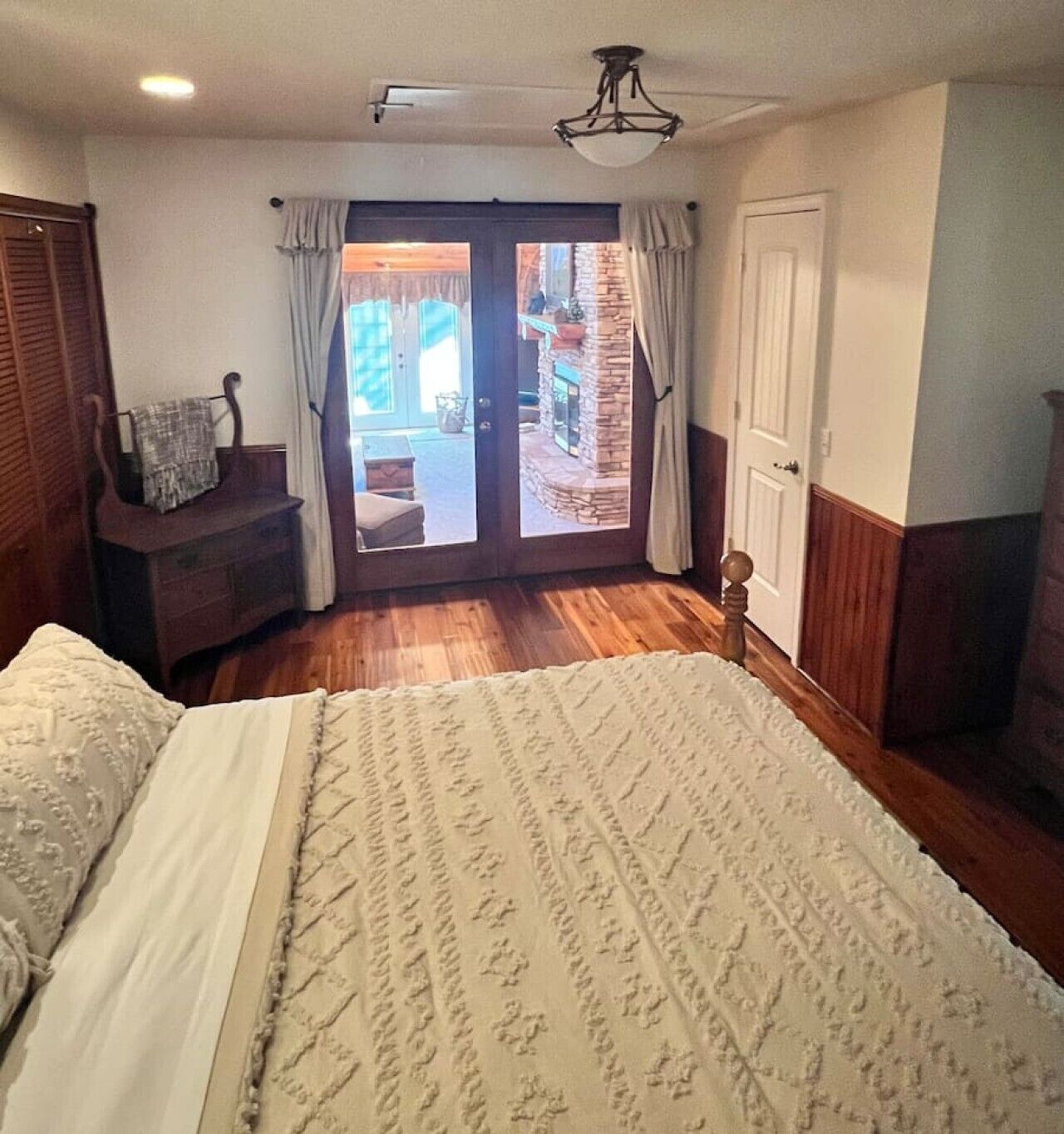 Een slaapkamer met een bed, een houten nachtkastje, een stoel, een deur en uitzicht op het omliggende landschap.