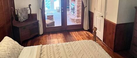 A bedroom with a bed, a wooden nightstand, a chair, a door, and a view of the outside.