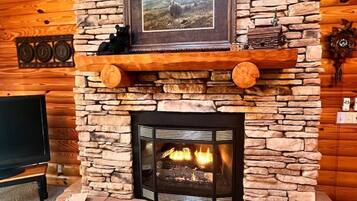 A stone fireplace with a framed picture above it, a clock on the wall, and a television in the corner.