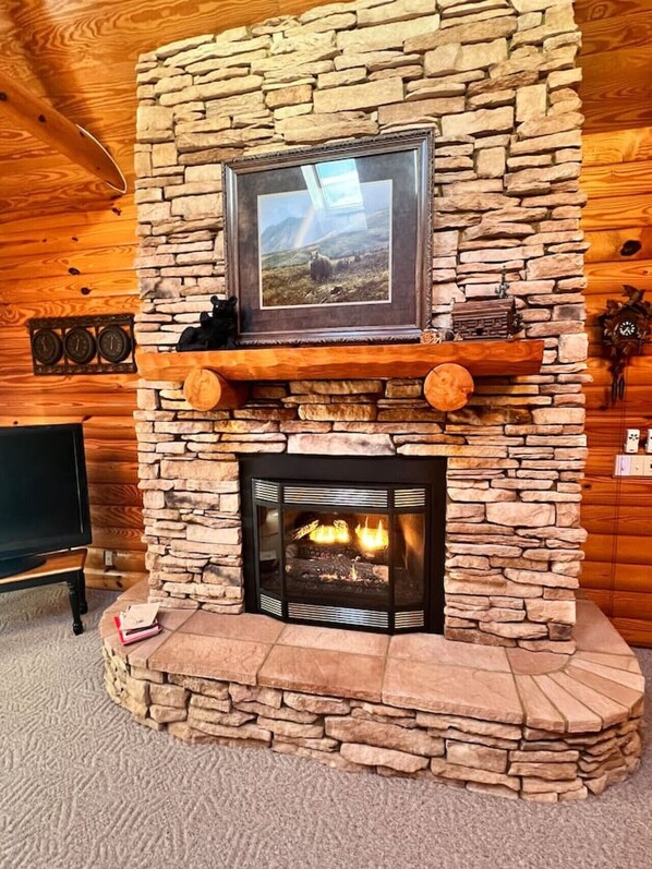 A stone fireplace with a framed picture above it, a clock on the wall, and a television in the corner.