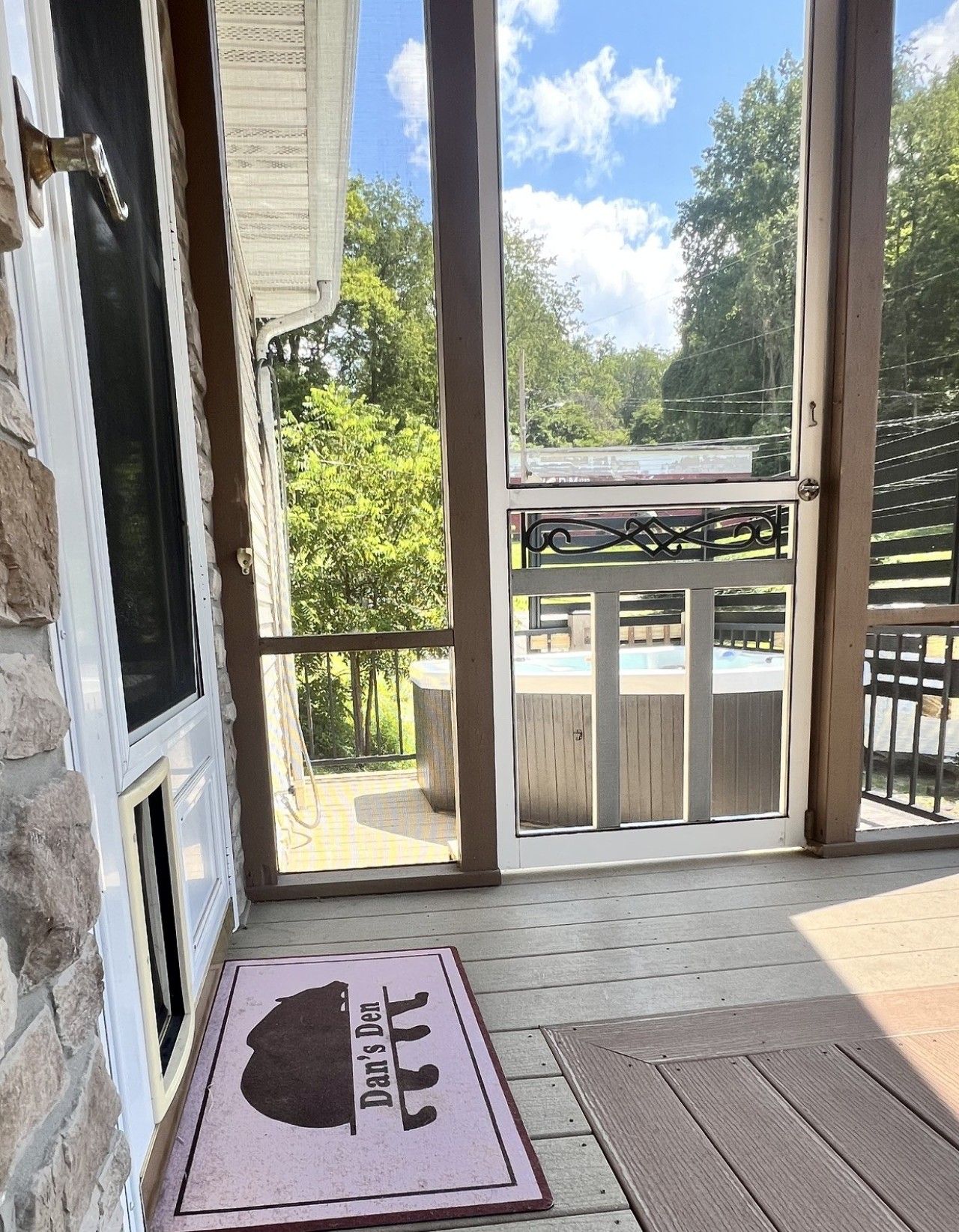 Un porche cubierto con un felpudo, vista a un patio trasero con piscina y una terraza de madera.