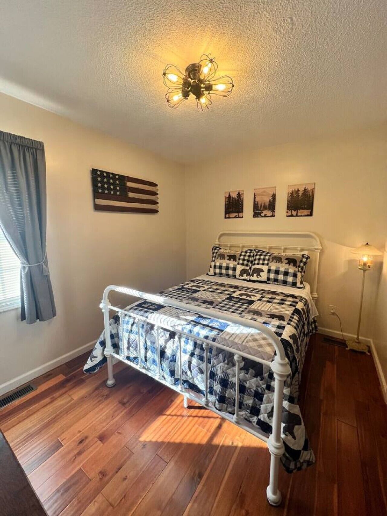 Un dormitorio con cama, lámpara de techo, ventana con cortinas y decoración en las paredes.