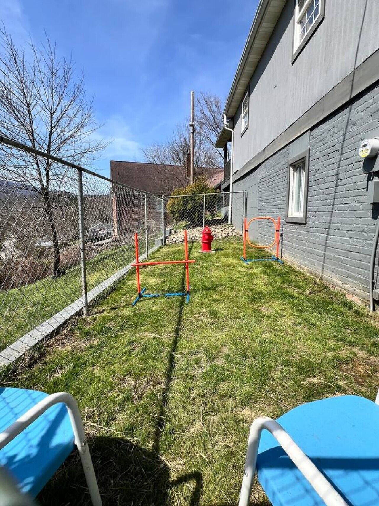 Une cour clôturée avec une zone herbeuse, un potelet d’hydrant rouge et un bâtiment doté d’une fenêtre et d’un coffret de raccordement.