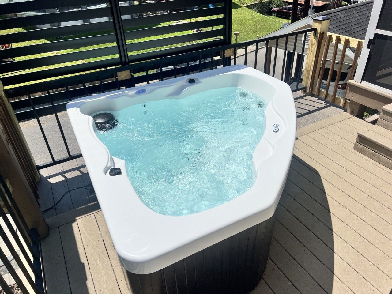 A hot tub on an outdoor deck with a wooden railing and a view of a residential area in the background.