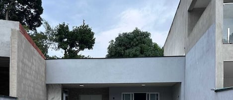 Un área de piscina moderna al aire libre, con una piscina azul cristalina, un espacio de estar techado con sillas y un edificio de techo plano.