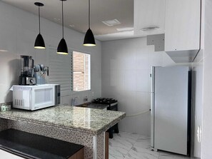 A kitchen with a granite countertop, a white microwave, a black blender, a gas stove, and a stainless steel refrigerator. - 3-bedroom house in marvelous Bertioga with AC and comfort (Bertioga)