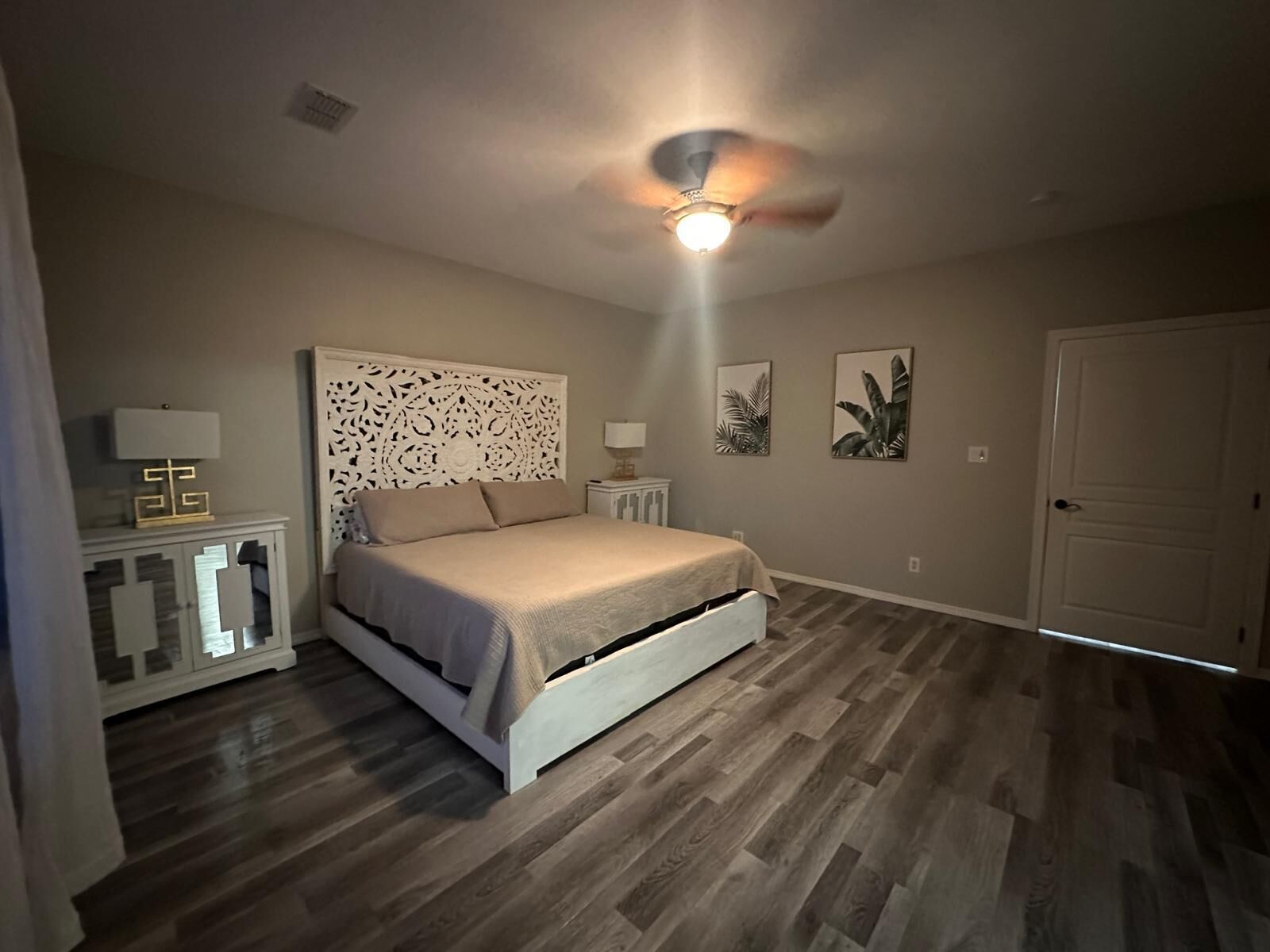 A bedroom with a bed, a ceiling fan, a nightstand, and a door.