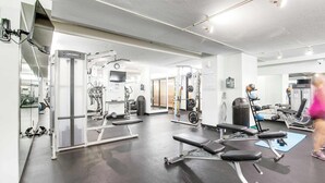 Un gimnasio con máquinas de pesas, bancos y un espejo.
