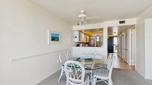 A dining area with a glass table and white chairs, a ceiling fan, and a kitchen visible through an open door. - Sea Colony - 603N Edgewater House (Bethany Beach)