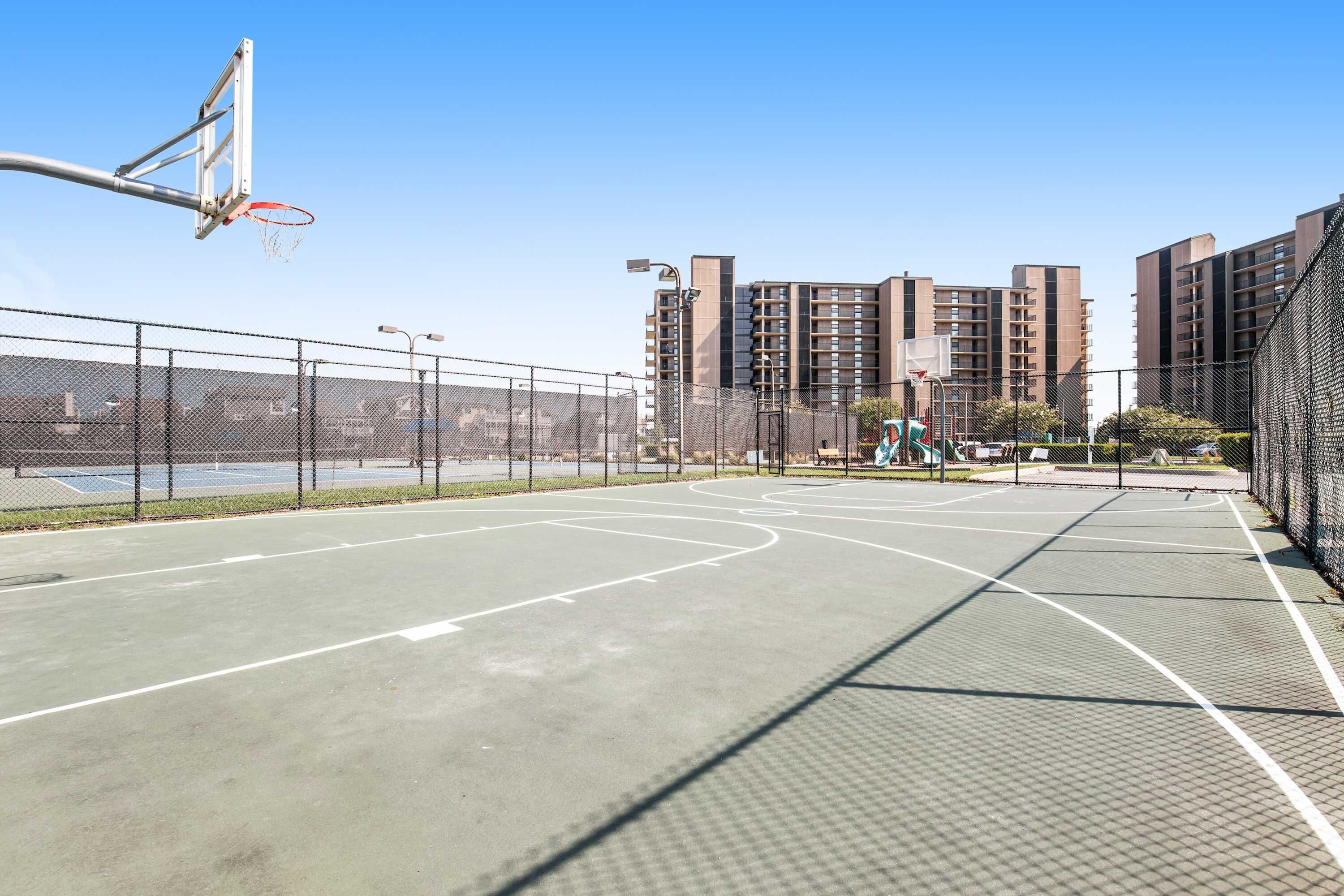An outdoor basketball court with a net, surrounded by a fence, and adjacent to a building.