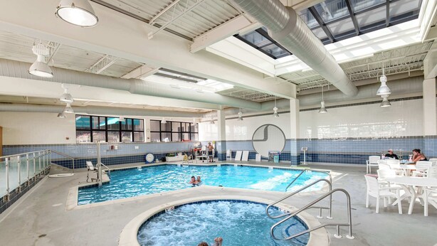 Una piscina interior con hidromasaje, zona de descanso y vistas de la ciudad a través de amplios ventanales.