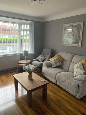 Ein Wohnzimmer mit grauem Sofa, einem Holztisch und einem Fenster mit Jalousien.