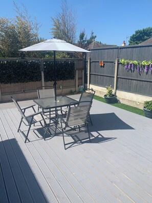 A patio with a table and chairs, surrounded by a wooden fence and greenery.