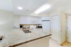 A kitchen with white cabinets, a granite countertop, a stove, a microwave, and a refrigerator. - Carolinian Beach Resort 1934 (Myrtle Beach)