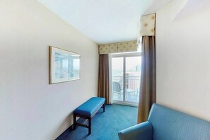A hotel room with a large window, a blue sofa, a small bench, and a framed picture on the wall. - Carolinian Beach Resort 1934 (Myrtle Beach)