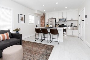 A modern kitchen with white cabinets, stainless steel appliances, and a central island with bar stools. - The Inn at 201 Fulton St. (Sandusky)