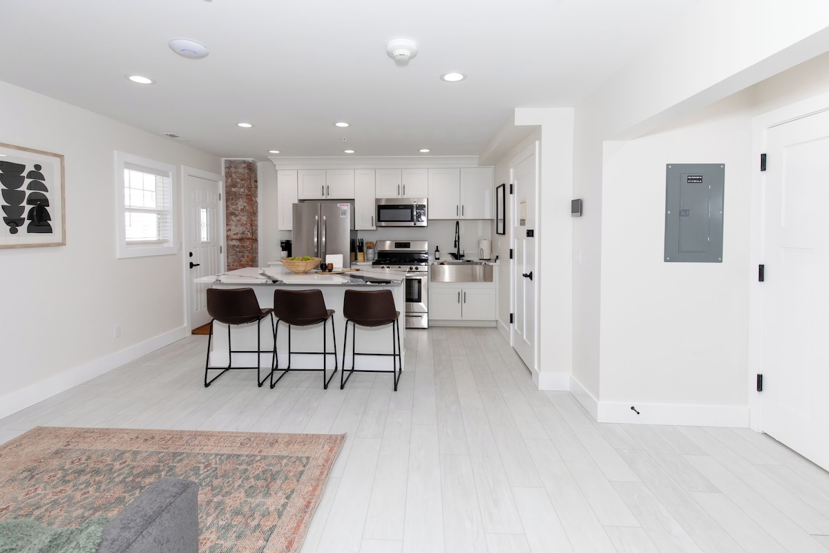 A modern kitchen with white cabinets, a central island with bar stools, and stainless steel appliances.