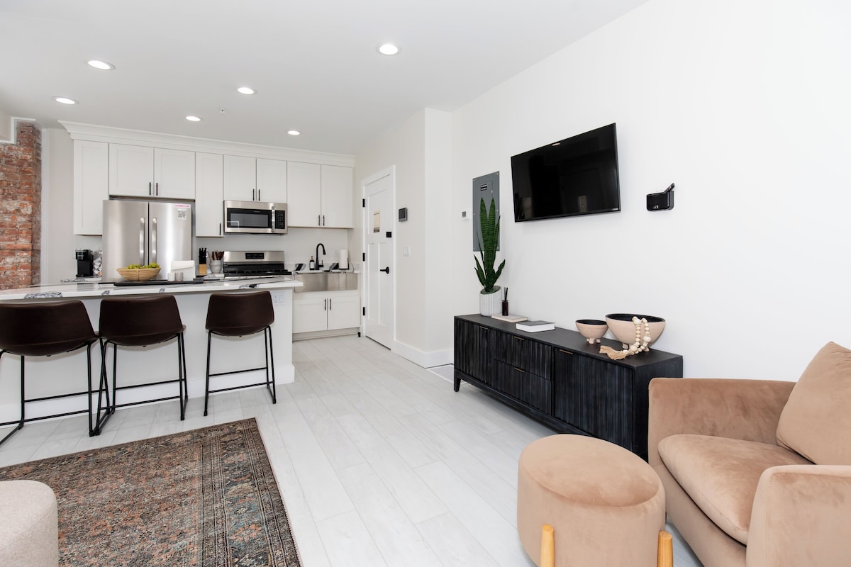 A modern kitchen with white cabinets, a black countertop, and a stainless steel refrigerator.