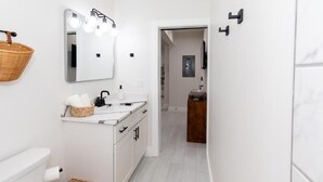 Un baño moderno con un tocador blanco, un espejo con luces, una cesta y una toalla.