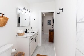 A modern bathroom with a white vanity, a mirror with lights, a basket, and a towel. - The Inn at 201 Fulton St. (Sandusky)