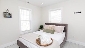 Un dormitorio con cama, mesita de noche con una planta y ventana con persianas.