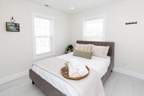 A bedroom with a bed, a bedside table with a plant, and a window with blinds. - The Inn at 201 Fulton St. (Sandusky)