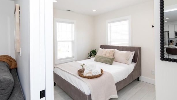 Un dormitorio con cama, mesita de noche, espejo y ventana.
