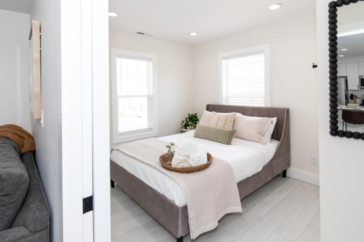 A bedroom with a bed, a bedside table, a mirror, and a window.