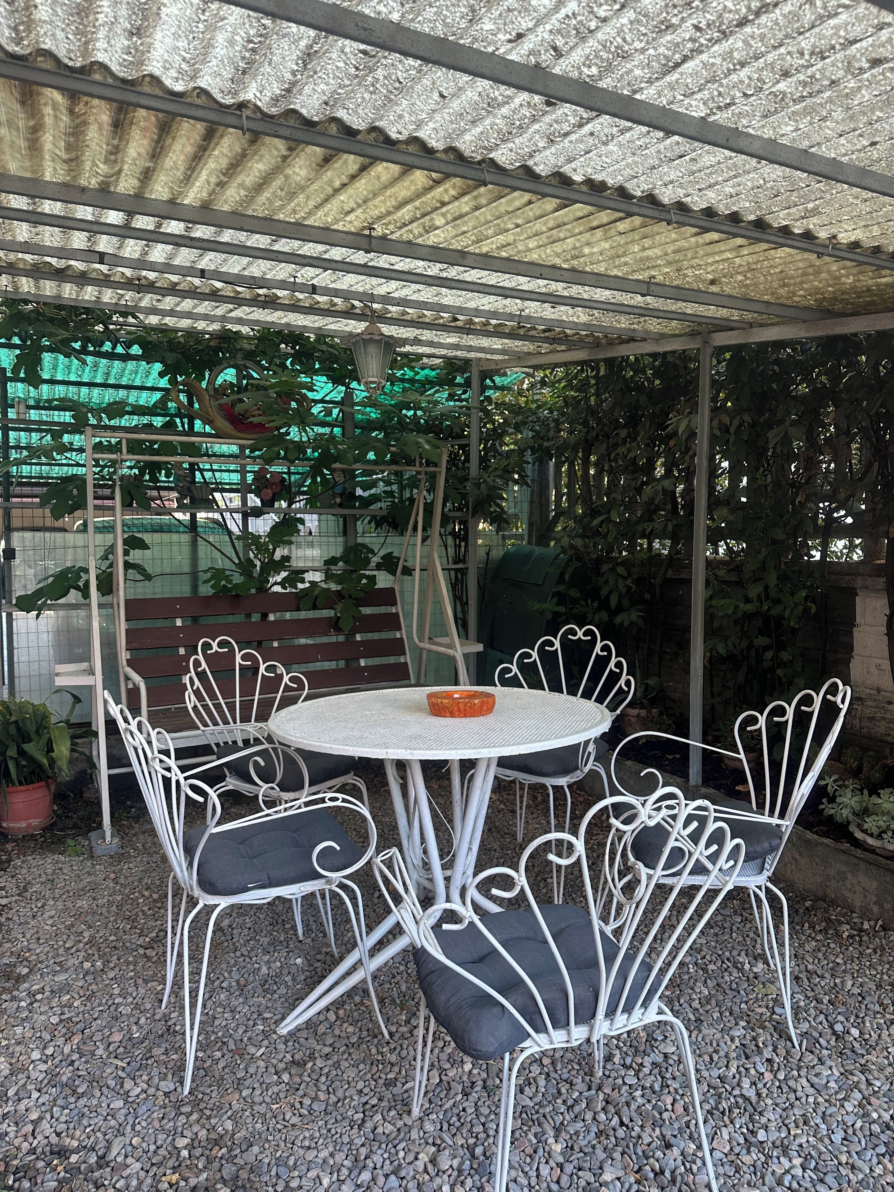 A covered outdoor seating area with a round table and white metal chairs.