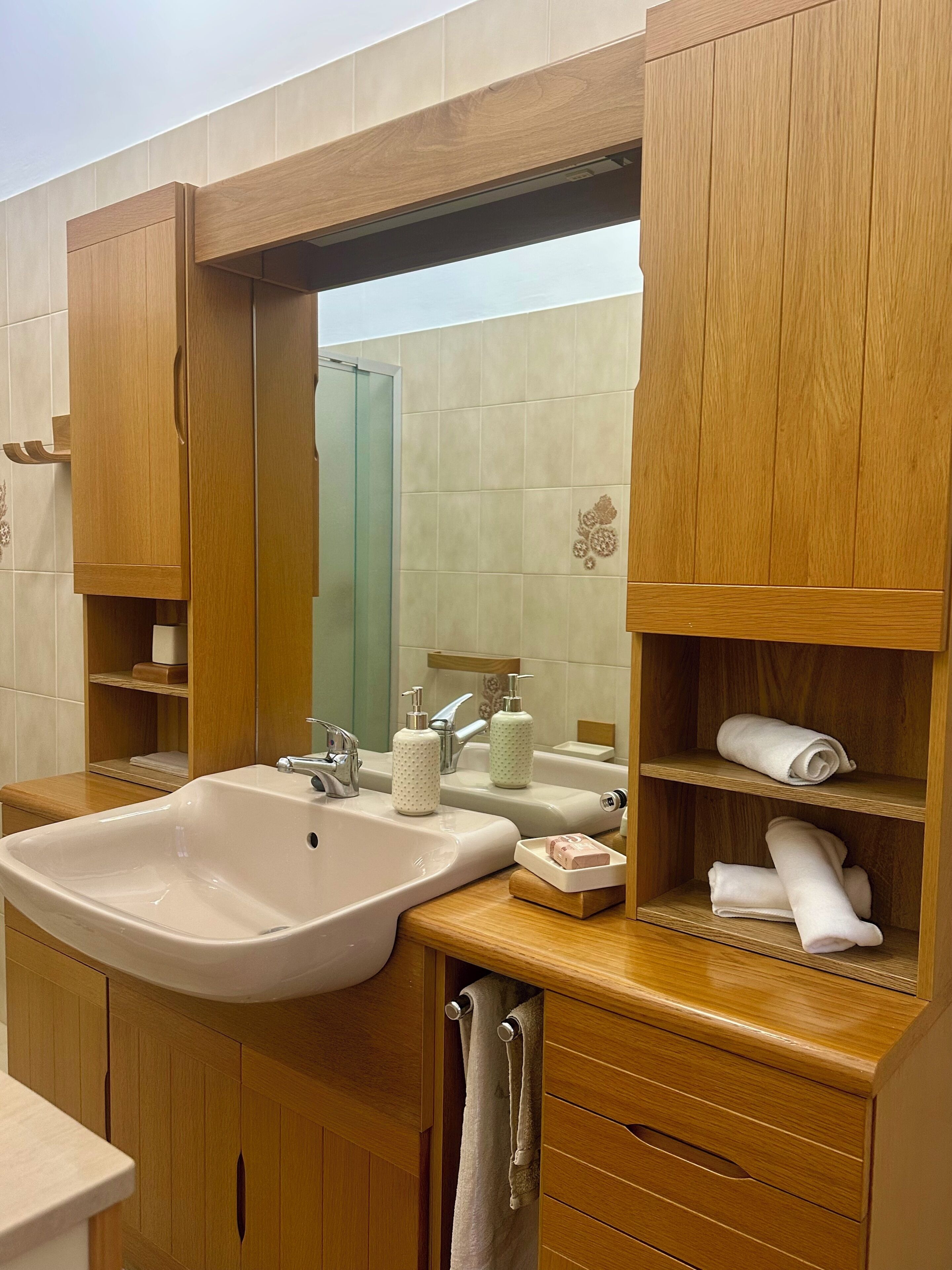 A bathroom with wooden cabinets, a large mirror, a sink, and a towel rack.