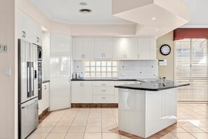 Eine moderne Küche mit weißen Schränken, einem eingebauten Backofen, einem Edelstahlkühlschrank und einem Fenster mit Jalousien.