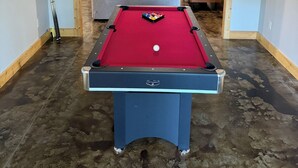 Ein Billardtisch mit Spielzeug, eine Couch und ein Fernseher in einem Raum mit Betonboden.