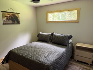 Um quarto com uma cama, uma mesa de cabeceira, uma janela e um quadro na parede.