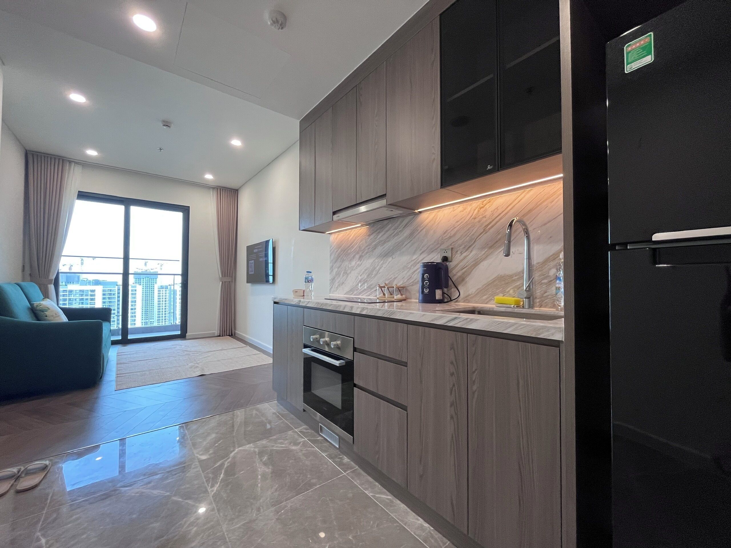 A modern kitchen with dark cabinetry, a black refrigerator, and a marble countertop.