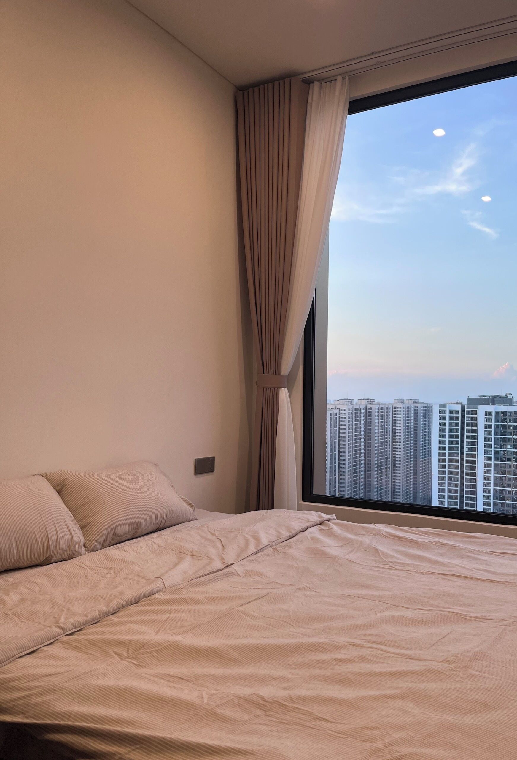 A bedroom with a large window, a bed, and curtains.