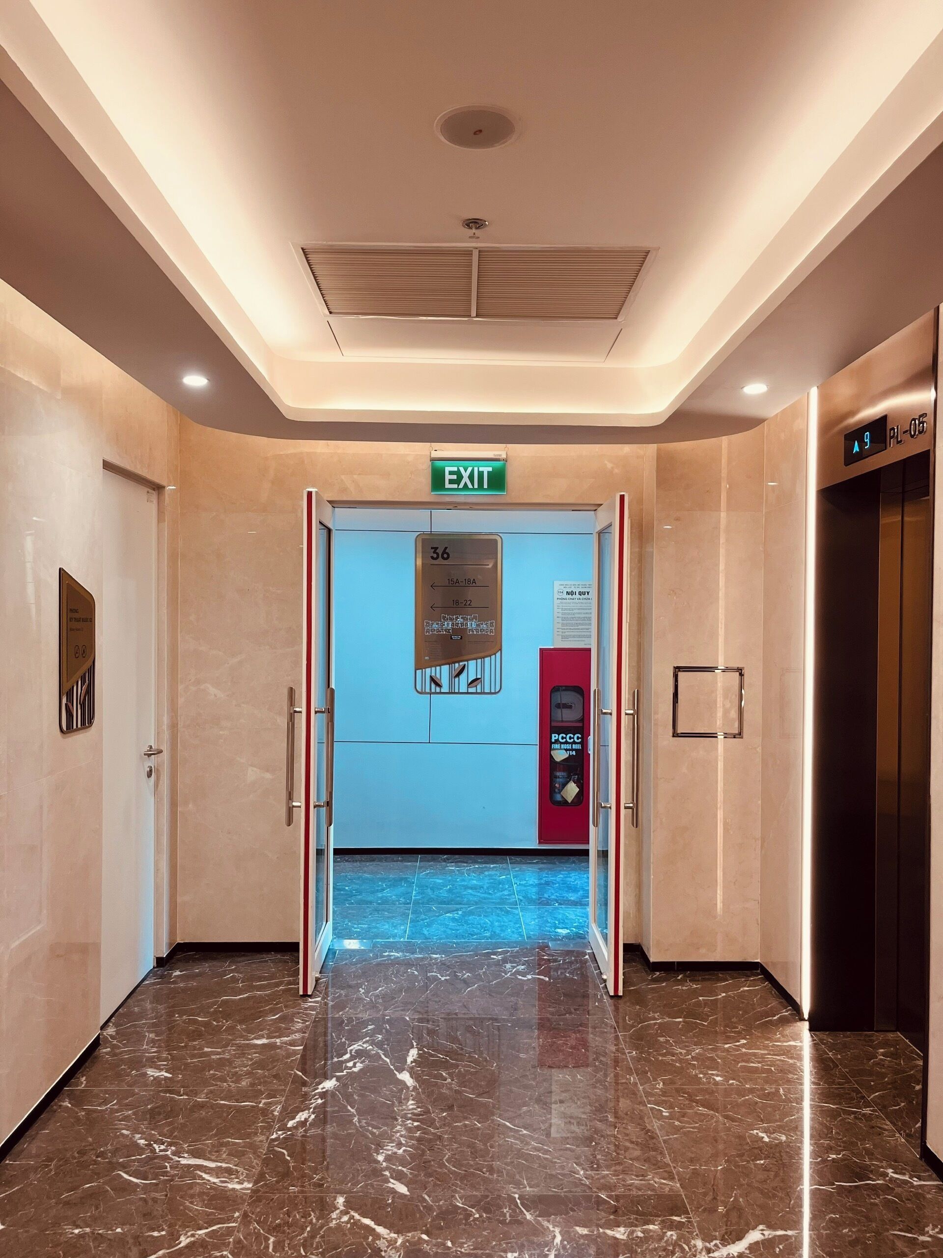 A hotel corridor with an exit sign, an elevator, and a blue wall with a sign.