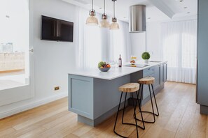 Una cocina moderna con una isla grande, luces colgantes, un televisor de pantalla plana y vistas a la ciudad.